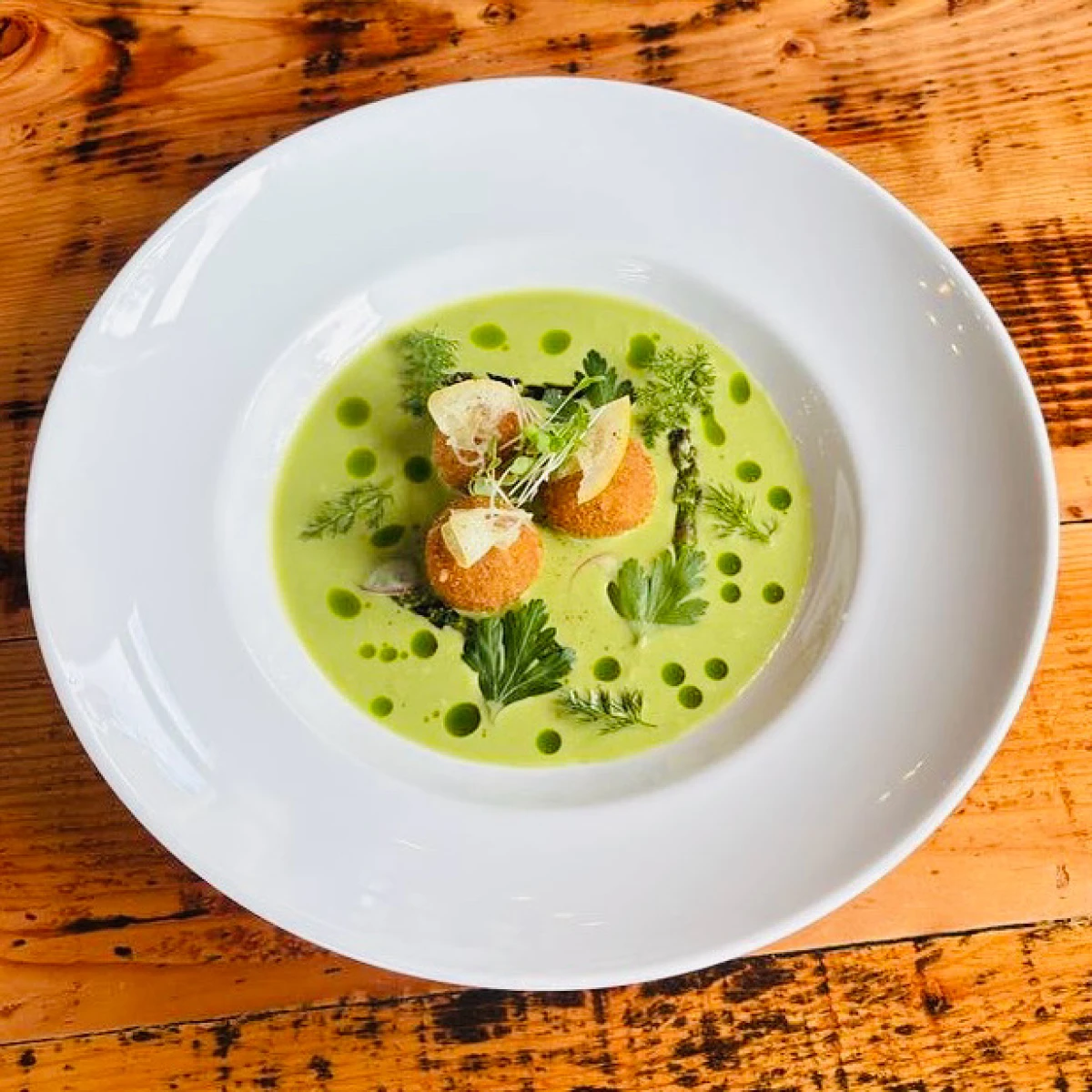 Two round, golden-brown crab cakes topped with a colorful mix of diced vegetables and sprouts, served on a dark slate plate with dollops of creamy sauce and a decorative swipe.