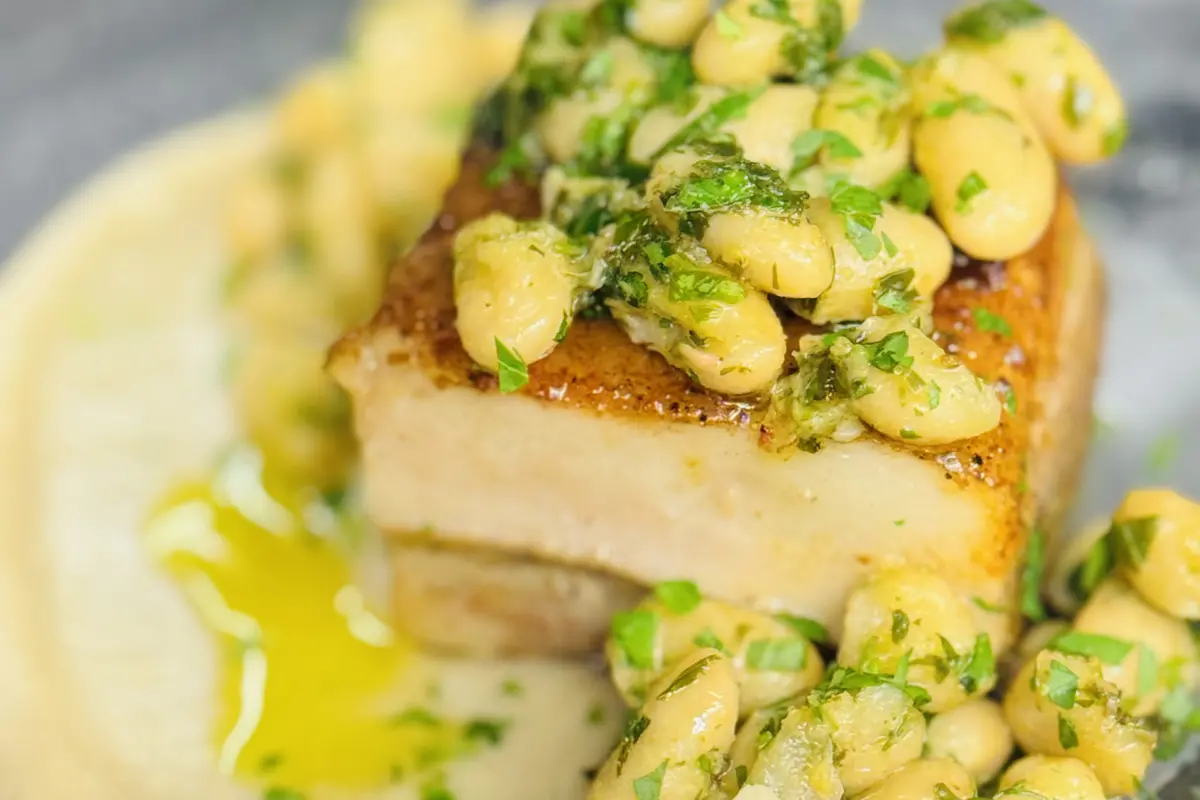 Three plates of food are presented on a stainless steel countertop, likely in a commercial kitchen. Each plate features a neatly arranged serving of salad with green leaves, topped with a breaded and fried item garnished with orange fish roe. The focus is on the first plate, making the details clear while the other two plates gradually blur into the background.